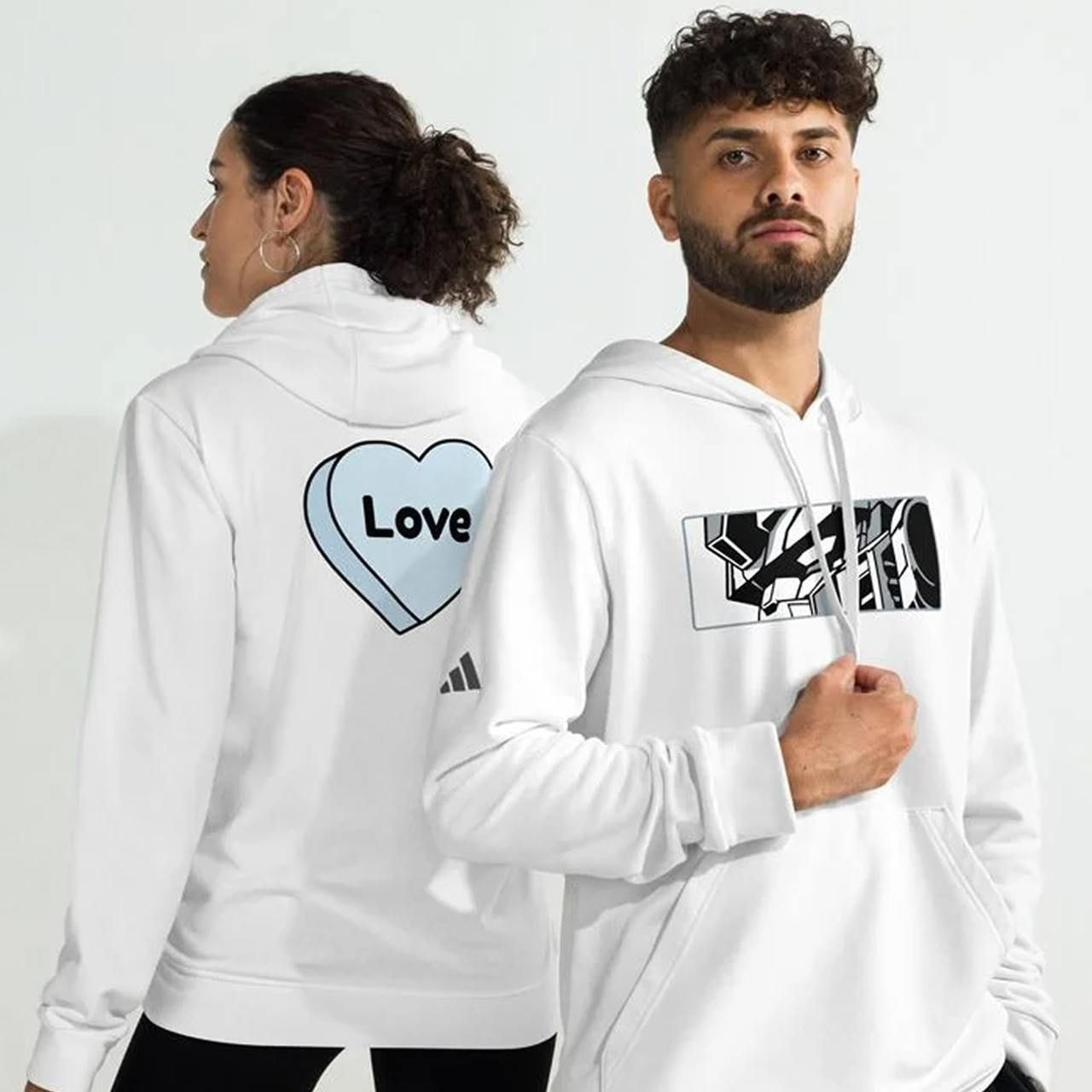 A man and woman wearing white adidas hoodies with illustrated prints.